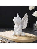 White angel ornament displayed on tray with flowers and candles.