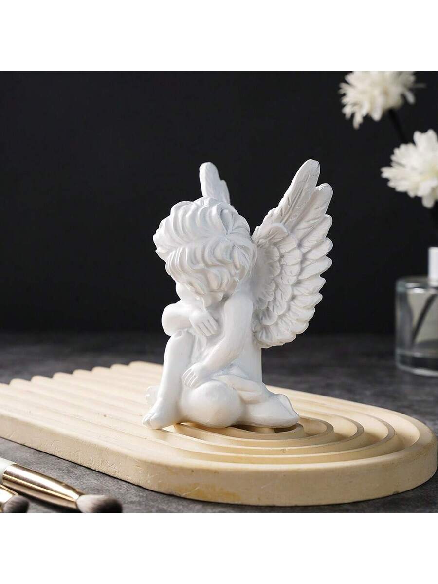 White angel ornament displayed on tray with flowers and candles.