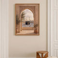 Gold toned framed Islamic wall art in a cream hallway showing the Kaaba crowd ornate arch and potted trees