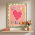 Framed pastel affirmation print reading you are so loved above crib and toys