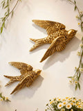 Pair of antique gold swallow wall sculptures mounted diagonally on cream wall.