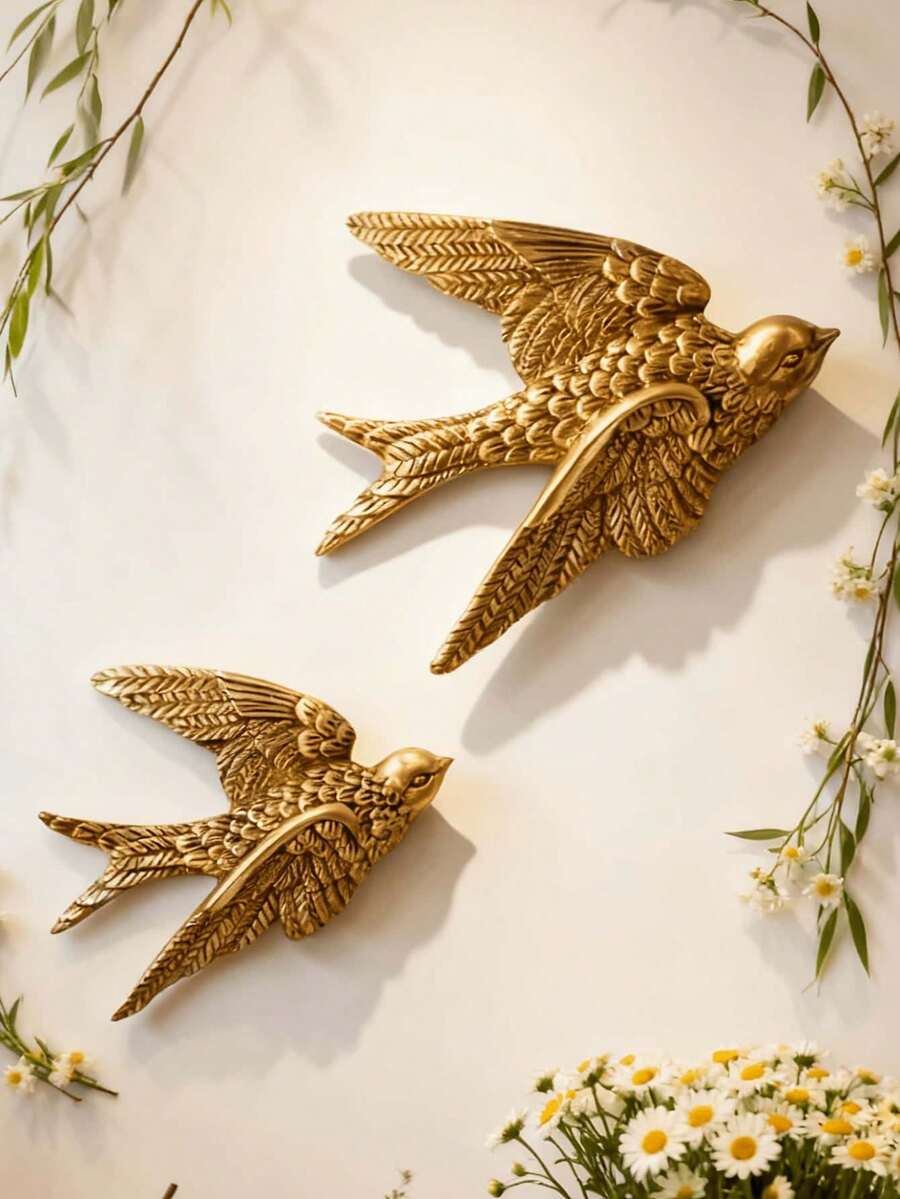 Pair of antique gold swallow wall sculptures mounted diagonally on cream wall.