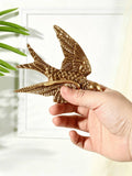 Gold bird wall accent styled near sofa, mirror, flowers, and plants.