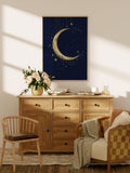 Light wood framed gold crescent moon wall art above a dresser with flowers books and candles in a warm living room