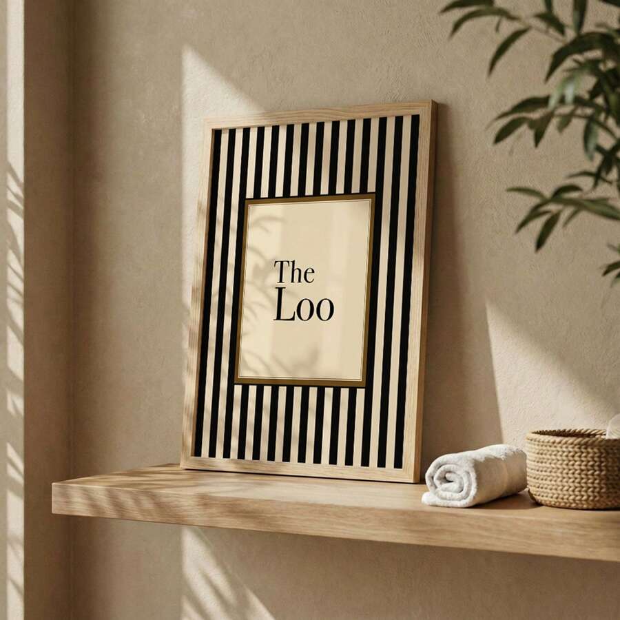 Framed The Loo bathroom art on wooden shelf with towel and woven basket