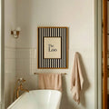 The Loo framed bathroom print above bathtub with brass fixtures and towels