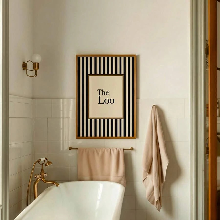 The Loo framed bathroom print above bathtub with brass fixtures and towels