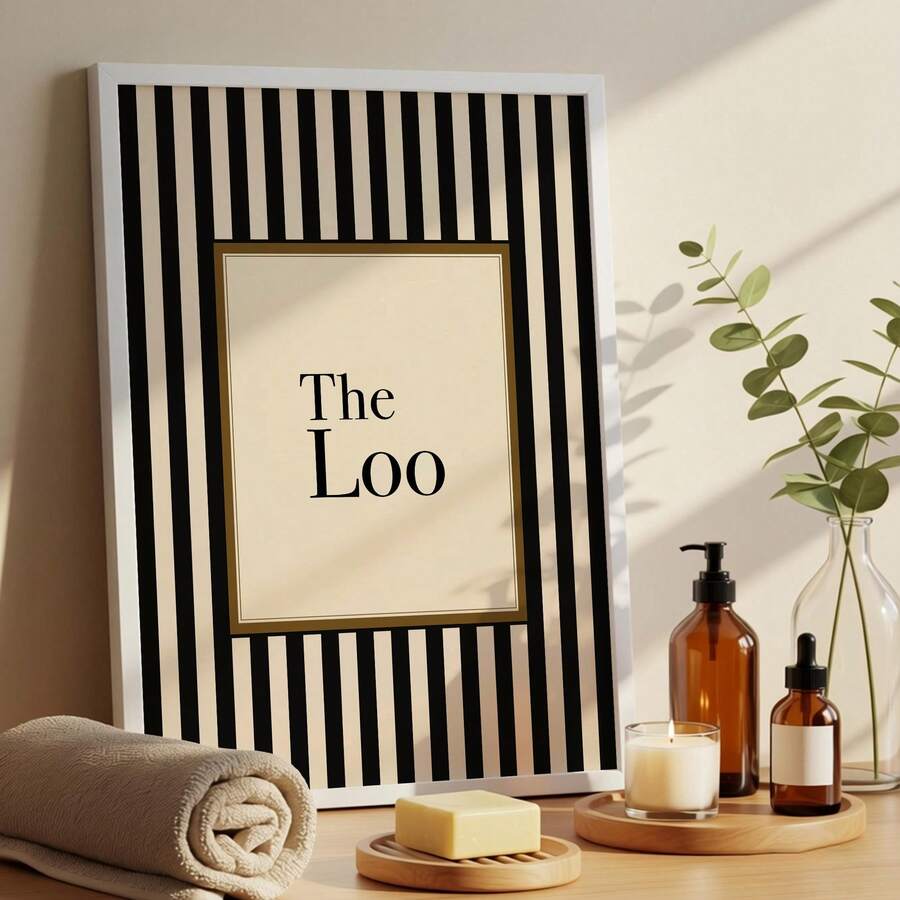 White framed The Loo print styled with towels soap candle amber bottles and greenery