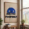 Framed funny ARE YOU POOPING print beside window with mountain view and small plants