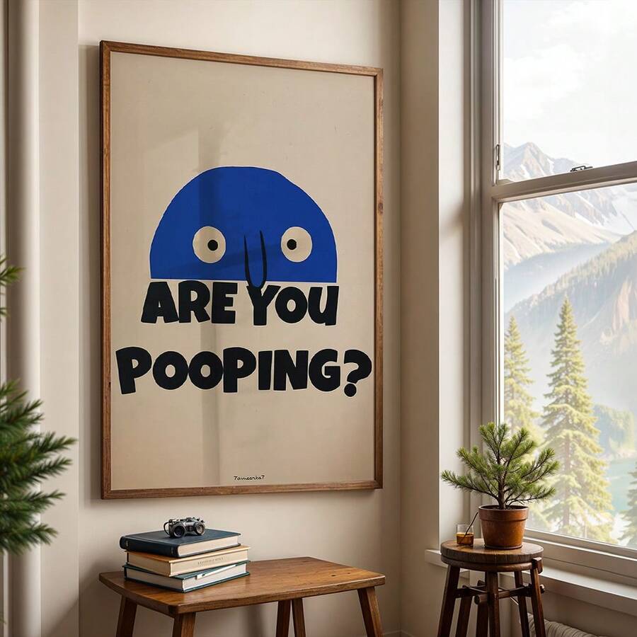 Framed funny ARE YOU POOPING print beside window with mountain view and small plants