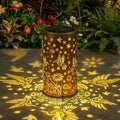 Solar metal lantern detail showing warm LED glow and perforated floral pattern.