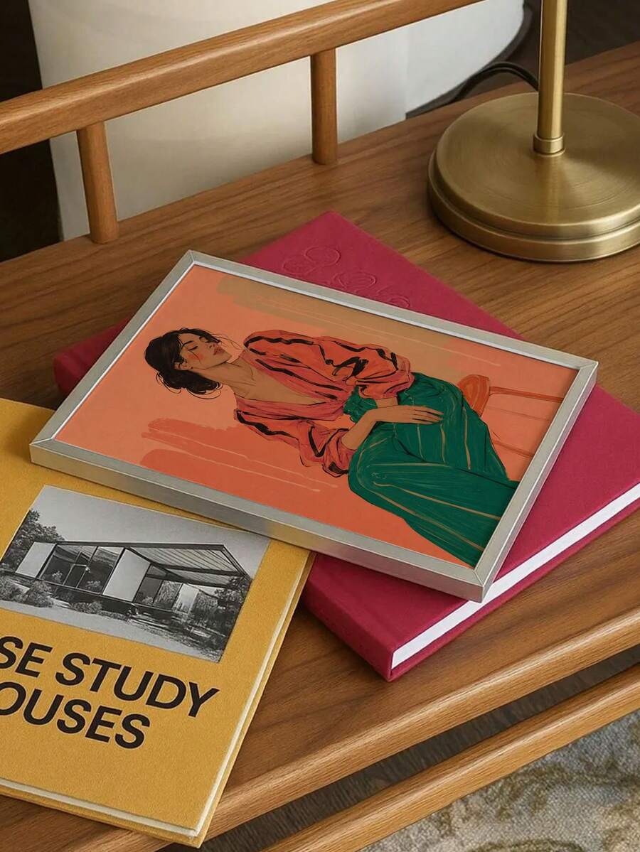 Silver framed seated woman print lying on books beside brass lamp