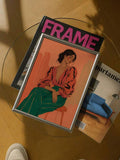 Silver framed fashion illustration on glass table with FRAME magazine