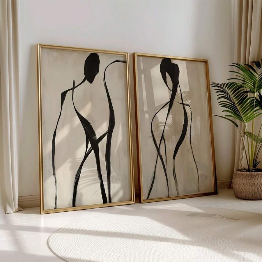 Two gold framed abstract figure prints leaning on floor beside plant and curtains