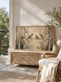 room mockup view of Rustic nature canvas wall art showing three birds on a branch, birch trees, woodland foliage, warm beige neutrals and soft painterly cottage style.
