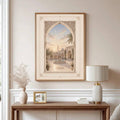 Wood framed pale courtyard wall art above a console with an ornate arch fountain and crescent sky