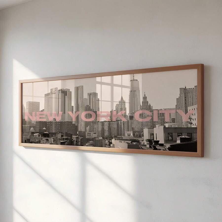 front framed view of Panoramic framed wall art showing a black and white New York City skyline photo with blush pink NEW YORK CITY typography and modern travel poster style.