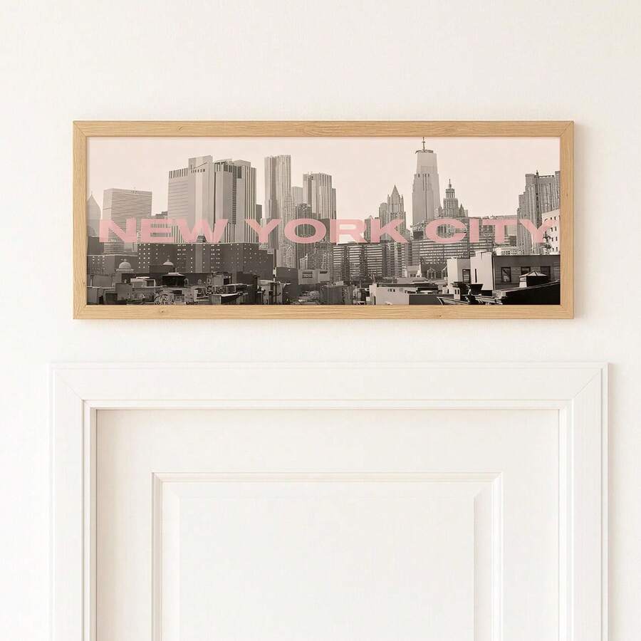 room mockup view of Panoramic framed wall art showing a black and white New York City skyline photo with blush pink NEW YORK CITY typography and modern travel poster style.