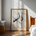 Wood framed two crane ink sketch poster leaning on bedroom wall in sunlight