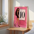Framed pink fashion doll 10 score poster leaning on bedside table in sunlit bedroom