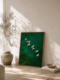Framed green bird print leaning beside vase and books in calm boho room