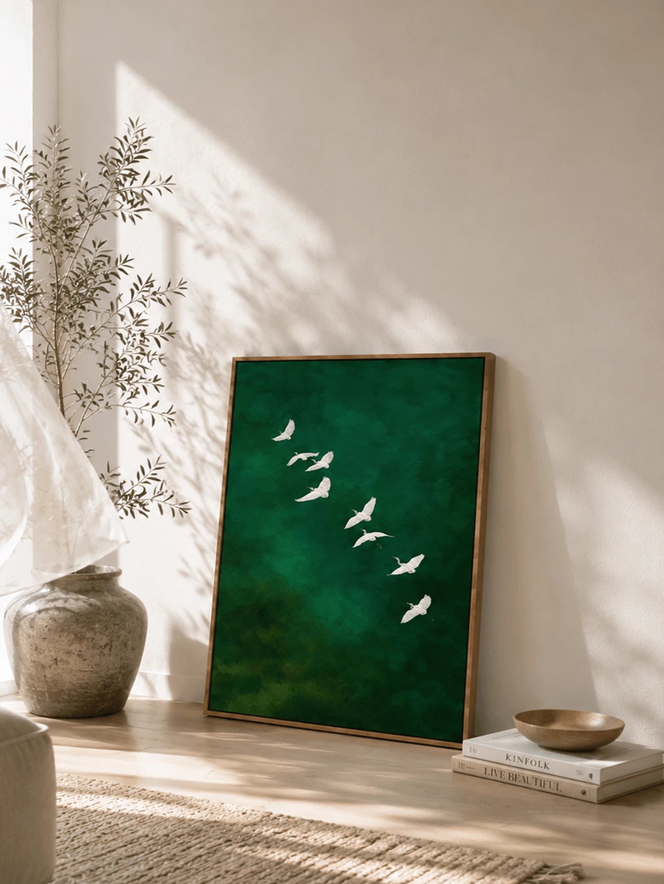 Framed green bird print leaning beside vase and books in calm boho room