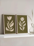 Two framed olive green botanical flower prints on white shelf beside clear glass vase with tall grass