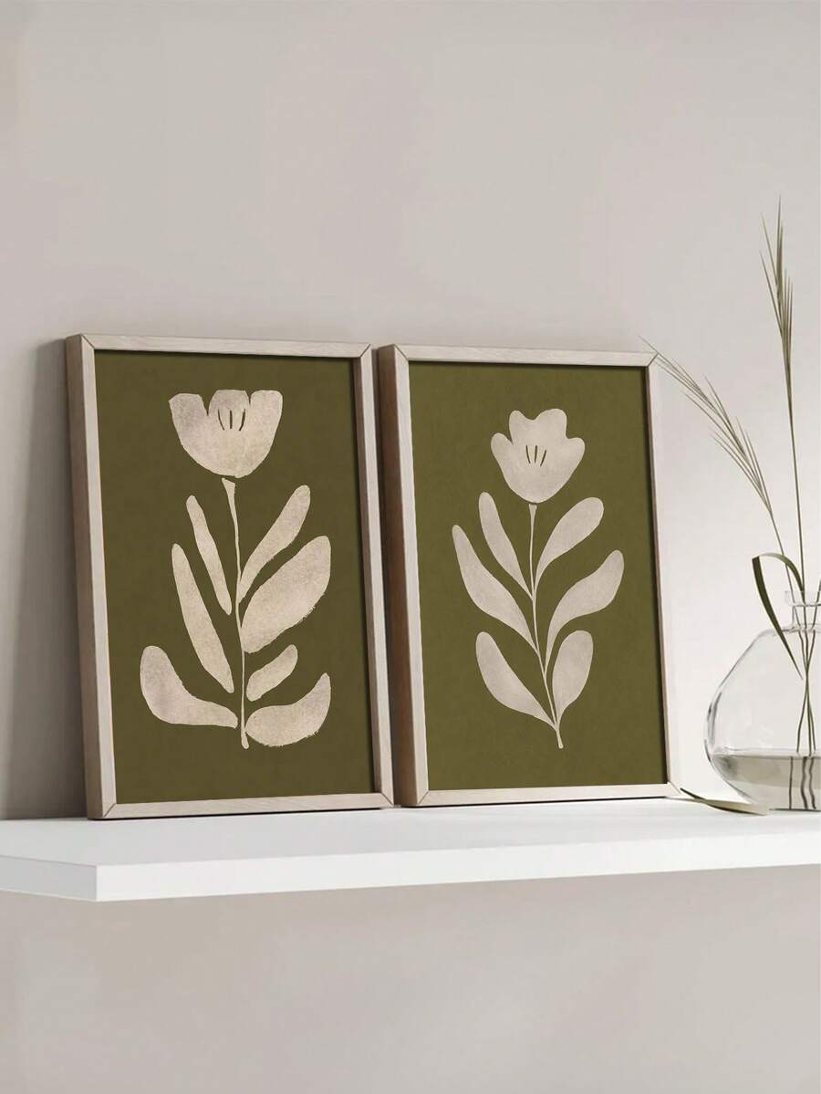 Two framed olive green botanical flower prints on white shelf beside clear glass vase with tall grass