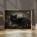 Large gold framed black cat meadow print leaning on floor with cat nestled in dark wildflowers under soft window light