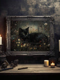 Ornate framed dark pastoral poster of black cat lying in wildflower meadow with candles and gothic tabletop decor