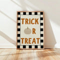 Trick Or Treat plaid Halloween poster in light wood frame leaning against cream wall with sun shadows