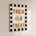 Wall mounted Trick Or Treat Halloween poster in slim gold frame with orange text pumpkin icon and black checker border