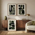 Two olive abstract prints hung with a third leaning beside a walnut credenza