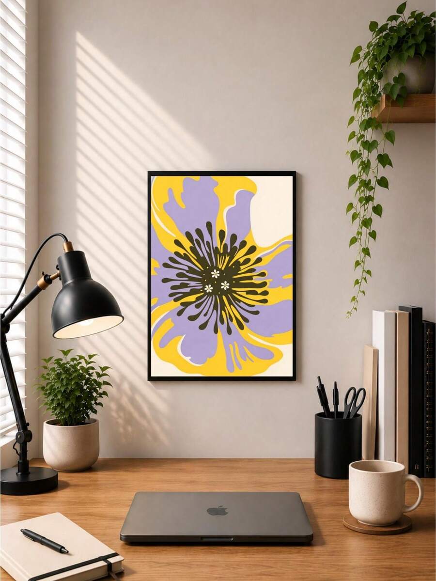Black-framed abstract flower print mounted above a wooden home-office desk and laptop