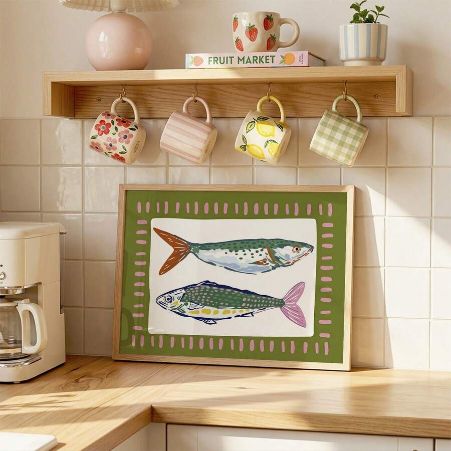 Framed folk-art fish print leaning on kitchen counter beneath patterned mugs