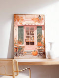 Framed pink pumpkin spice cafe autumn print on wooden desk beside white vase and cane chair