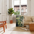 Tropical monstera wall art leaning beside beige sofa in bright living room with potted plant