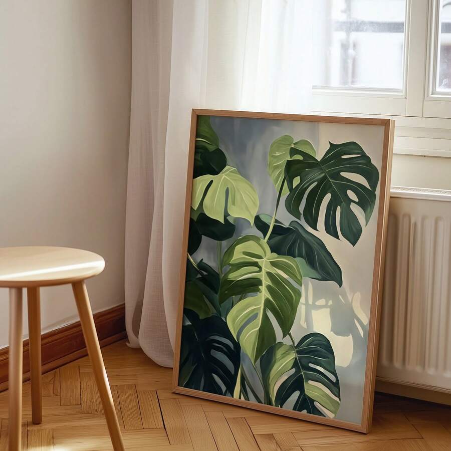 Framed green monstera leaf poster leaning by window and radiator beside wood stool