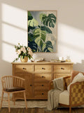 Monstera tropical botanical print hanging above wood dresser in warm neutral furnished room