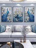 Three blue peacock and floral vase wall prints above white sofa with blue pillows and chandelier