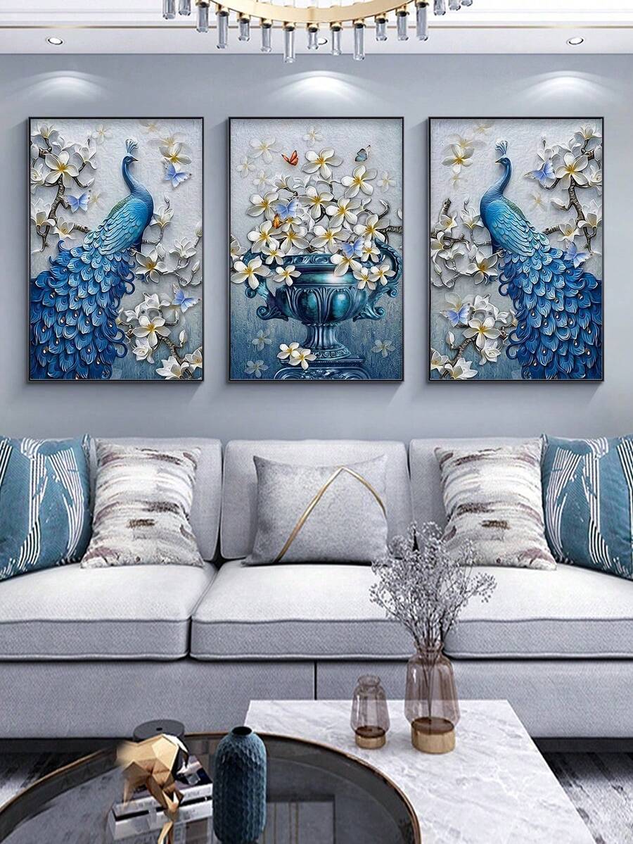 Three blue peacock and floral vase wall prints above white sofa with blue pillows and chandelier