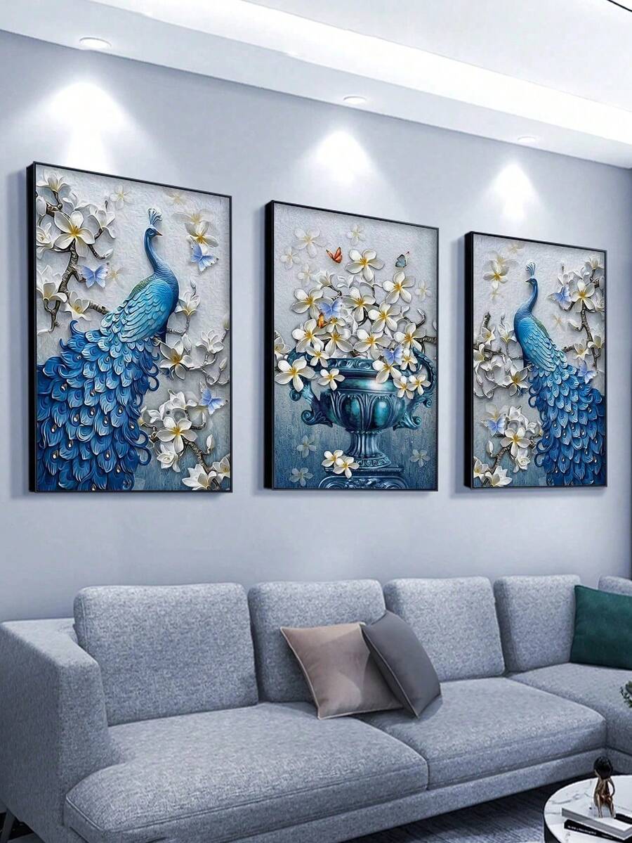 Three black framed blue peacock and white flower prints above gray sofa under spotlights