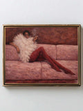 Gold-and-black framed reclining woman fashion poster displayed alone on pale wall