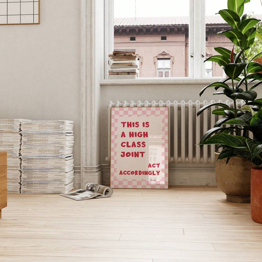 Small framed high class joint typography print below window beside magazines and green plants
