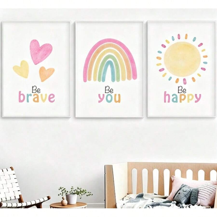 White-framed pastel wall art above nursery bed with Be brave hearts, Be you rainbow and Be happy sun