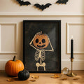 Pumpkin-headed skeleton Halloween artwork in a black display frame with orange and black pumpkins beneath a bat garland