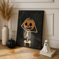 Pumpkin skeleton artwork in a black display frame beside pampas grass, a black pumpkin and a white ghost ornament