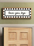 Black and white love you bye canvas sign displayed over doorway