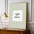 Gold-tone framed coffee please print with sage stripes beside a desk lamp