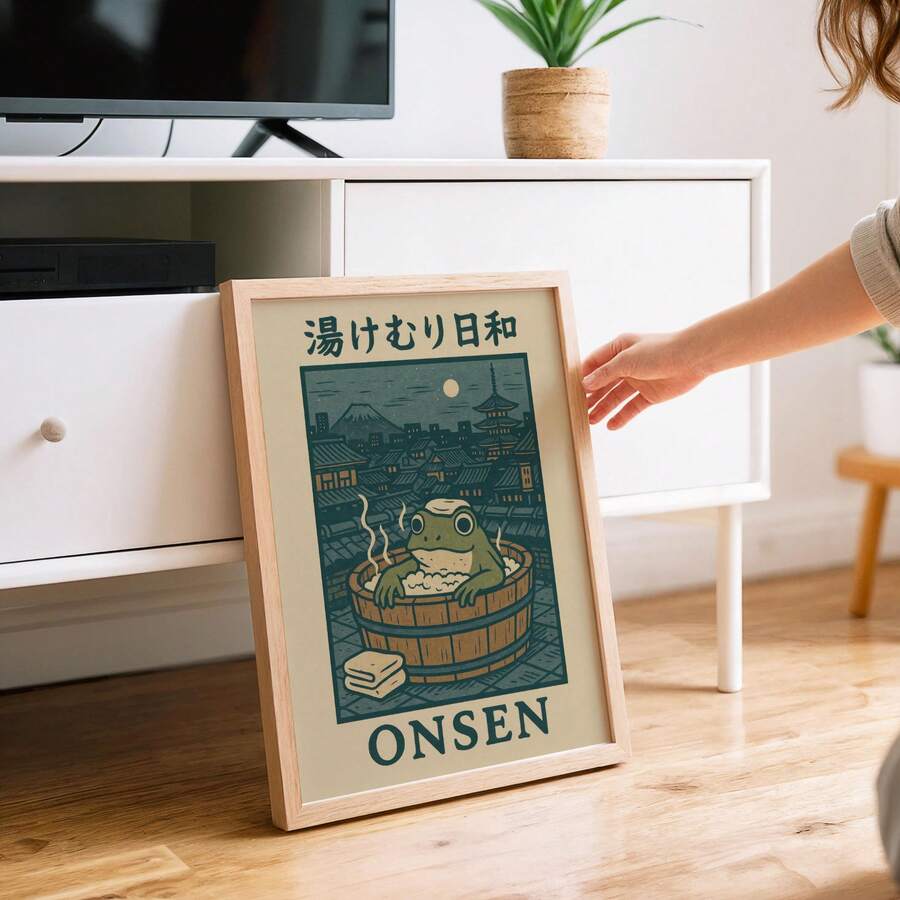 Person positioning a natural wood-look framed onsen frog print beside a white cabinet